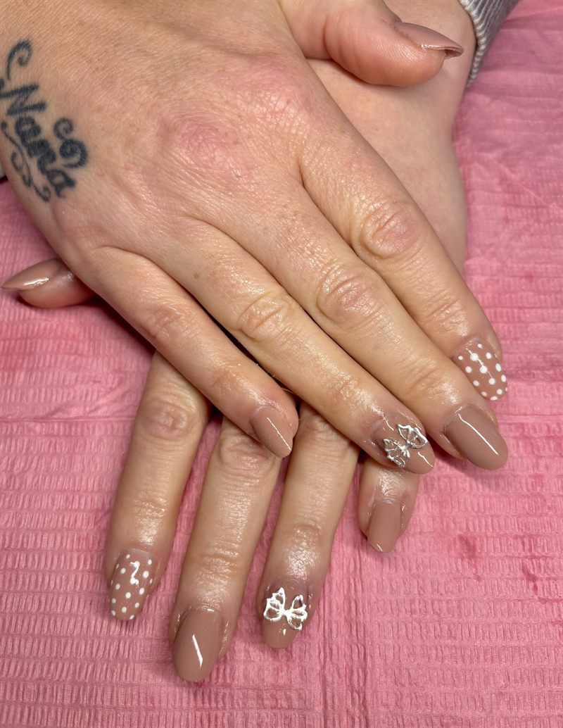 Nude gel nails with white polka dots and silver bows